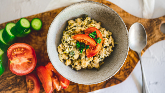 “Heart-healthy chickpea salad topped with tomatoes and herbs, served with fresh cucumber and tomato on a wooden board.”