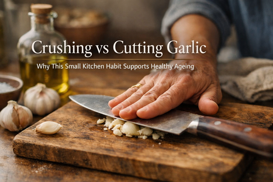 Hand crushing a garlic clove with the flat of a knife on a wooden board in a calm home kitchen